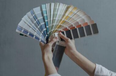 Hands displaying a fan of paint color swatches against a gray wall, ideal for home renovation projects.
