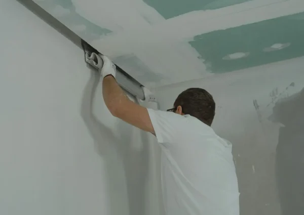 A man works meticulously on drywall installation during a house renovation.