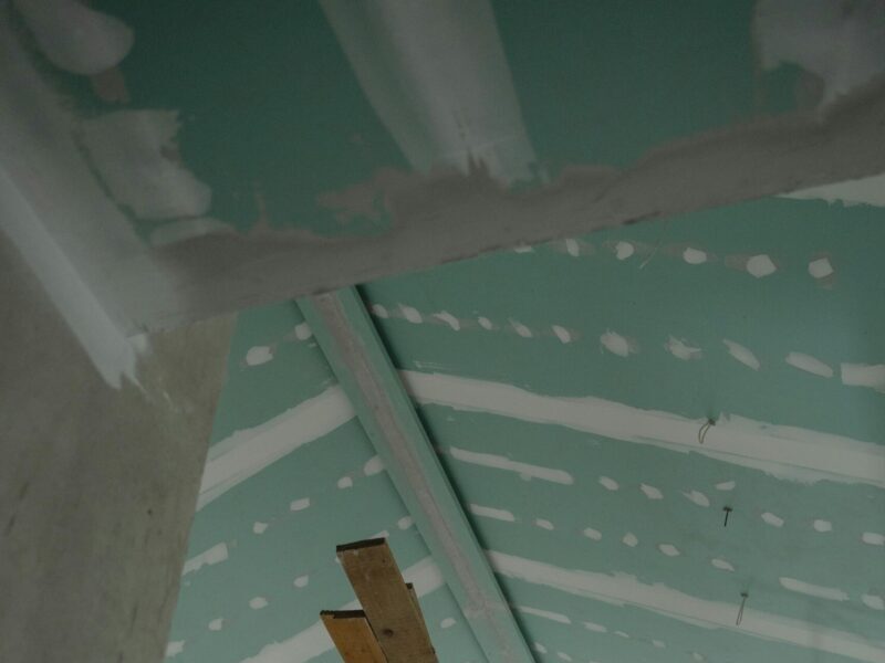 Scaffolding setup in an interior construction space with suspended ceiling boards and wooden planks.