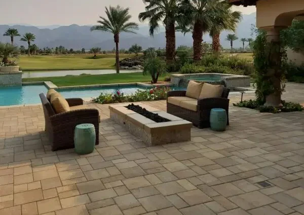 Serene outdoor patio with pool, wicker seating, and palm trees against mountain backdrop.